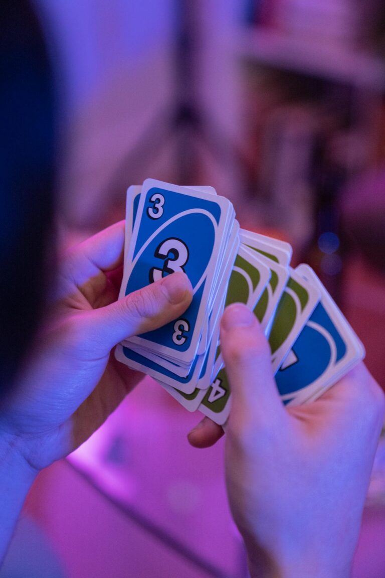 Hands holding and playing Uno cards with blue and green colors in focus.